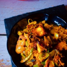 Dhaba Style Paneer Do Pyaza kept on a black plate with pan in the background