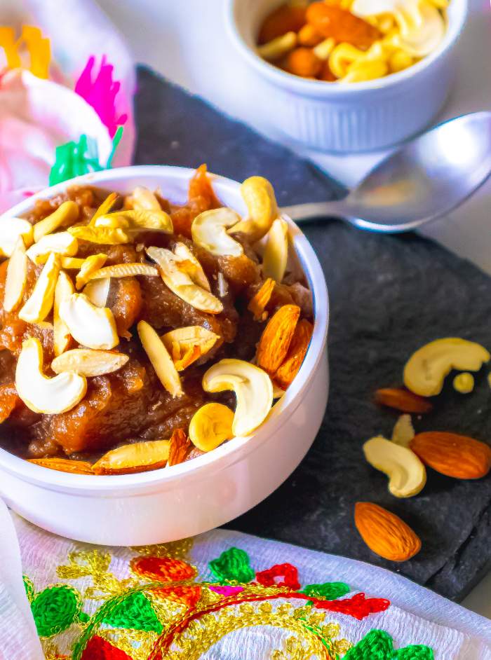 Singhare ka atte ka halwa kept in a white bowl with nuts strewn beside it and a spoon beside it