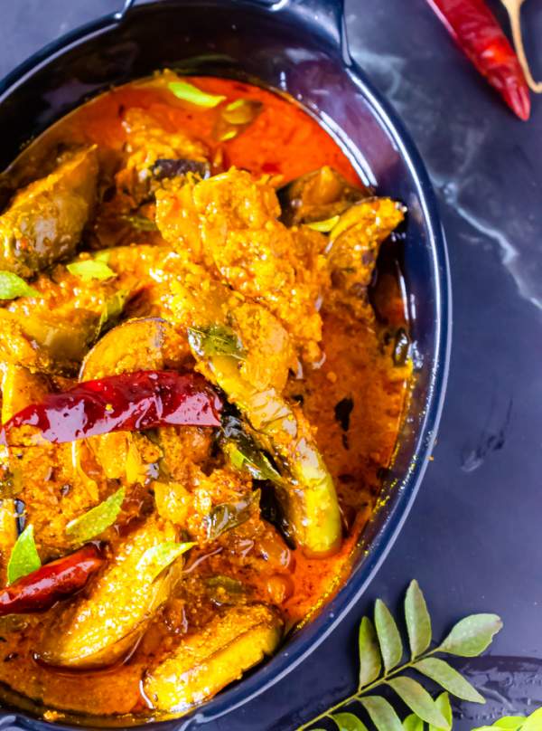 Bengali Dahi Baingan Recipe on a black plate with curry leaves beside