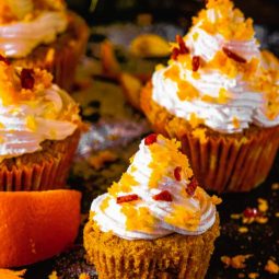 Orange Cranberry Cupcakes placed on a black background with Orange zest around